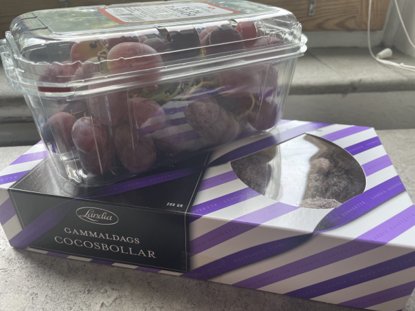 A purple and white striped box of “old fashioned” chocolate and coconut balls. A punnet of red grapes sits on top of the box. 