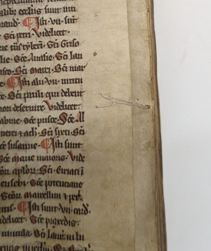 Parchment page with black manuscript. Red decorated letters. Beige thread attached in a v-shape. Thread twisted and projected from the foredges.