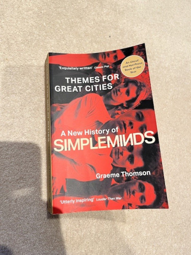 Cover of UK paperback of Themes for Great Cities. Cover has a black and red photo of the band, at a 90-degree angle, and the title of the book in white.