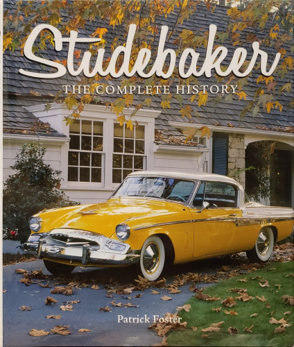 A photo of a large hardcover book. 
"Studebaker – THE COMPLETE HISTORY," by Patrick Foster.
On the cover, a photo of a sleek, bright-yellow '50s-vintage two-door coupe with whitewall tires, white detailing, and a lot of chrome. It's parked in front of nice home with white siding, dark shutters, stone details, and a steepled roof,. The branches of a tree are above the scene, full of colorful autumn leaves.