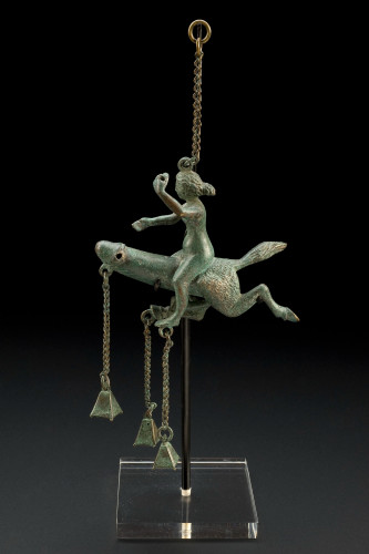 A woman riding a two-legged phallus. Roman wind chime made of bronze with bells hanging from the tip of the phallus and the woman's feet.