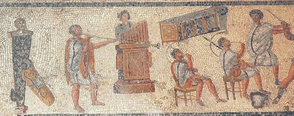 Part of a larger mosaic depicting from left to right: a herm with a shield propped up against it, a person playing a long pipe, a person playing a water organ, two men sitting down playing curved pipes, a man holding the arm of someone out of frame.