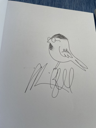 Ink drawing of a chubby little bird wearing round wire-rim glasses, on the blank page of a book. The borb is perched atop the B of Alison Bechdel's autograph.