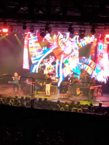 The Scottish band Belle and Sebastian performs at History in Toronto - This blurry but bright picture shows Sarah Martin, Stuart Murdoch and other band members in action, with colourful imagery projected behind the band. The heads of audience members in the front standing rows are visible in the bright light.