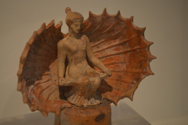 Terracotta figurine of Aphrodite, seated naked in an open sea shell.
