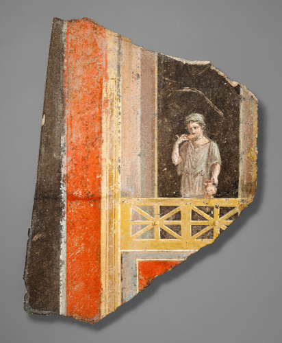 Description from the museum: “A young woman stands looking out from a balcony on this Roman fresco fragment. She wears a loose-fitting, sleeved tunic, cinched at the waist, along with a sakkos (cap), which matches the tunic’s light green color. She sips from a shallow cup held in her right hand, and balances an oinochoe (pitcher) on the railing of a balcony. The figure stands within an illusionistic architectural setting. Broad bands of black and red frame the scene at the left, and additional bands of color can be seen below the balcony.”