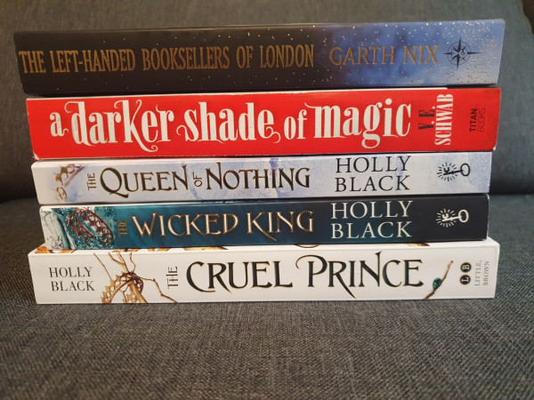 There are 5 books in the pile. From top to bottom: Carth Nix: The Left-handed Booksellers of London, V. E. Schwab: A Darker Shade of Magic, Holly Black: The Queen of Norhing, Holly Black The Wicked King and Holly Black The Cruel Prince
