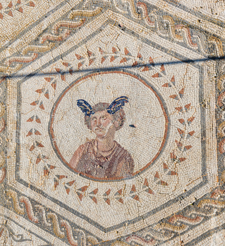 Mosaic detail of the Roman god Mercurius wearing a chlamys cloak pinned over his right shoulder and wings on his head. He is depicted inside a circle decorated with stylised laurel around it.