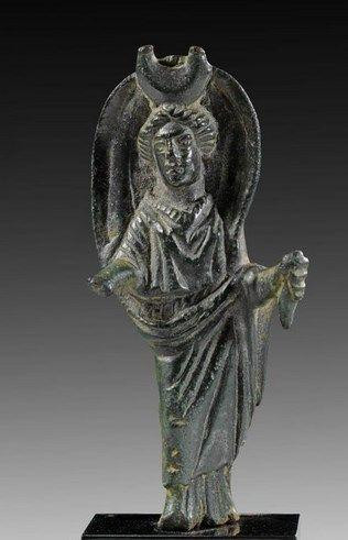 Charming little bronze figure depicting the moon goddess Selene with an appealing dark green patina. She has her iconic lunar crescent on her head and the billowing cloak behind her. Her left hand holds the remains of a torch. She is dressed in a long chiton with her himation cloak draped over her left arm.