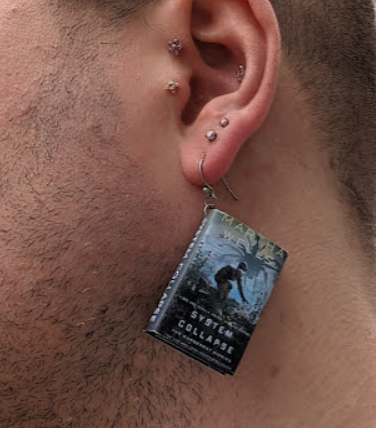 an earring that's a lil mini book for Martha Wells' "System Collapse"
