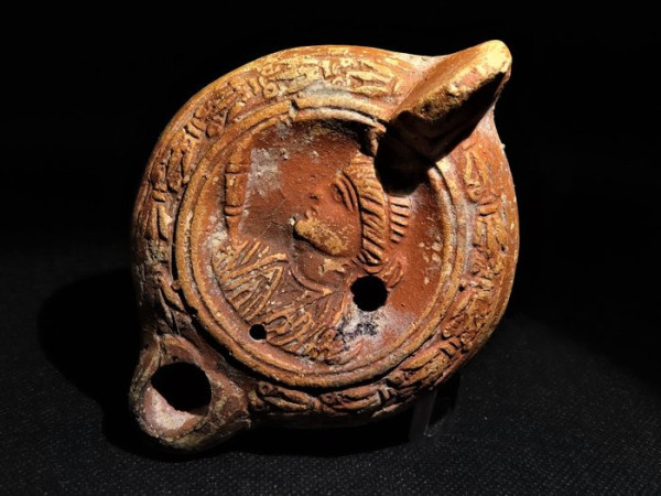 Roman terracotta oil lamp decorated with the bust of Luna. Her head is shown in profile, a torch, an iconic symbol of Selene and Luna, emerges at her right shoulder.