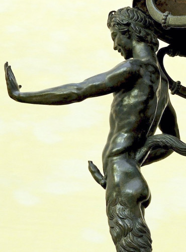 Detail of a satyr forming one of the legs of a bronze tripod. He has a visible erection and has lifted his left hand as if to make a modern stop gesture.
