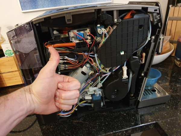Coffee machine with removed side cover and mechanism visible, a hand doing a thumbs-up in front 