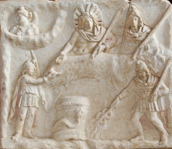 Relief of a banquet scene: In the middle, a bull's hide, of which the head and one hindleg are visible. Sol and Mithras recline on it side by side. Mithras holds a torch in his left hand and extends his right hand behind Sol. Sol is dressed only in a cape, fastened on his right shoulder with a fibula. Around Sol's head is a crown of eleven rays. He holds a whip in his left hand and extends the right towards a torchbearer who offers him a rhyton (drinking vessel). In the lower right is another torchbearer, with a torch raised in his left hand. In his right hand, he holds a caduceus into some water emerging from the ground. In the middle, an altar in the coils of a crested snake. In the upper left corner, Luna (the Moon) in a cloud, is looking away. Traces of red paint are still visible on the attire of Sol, Mithras and the torchbearers.