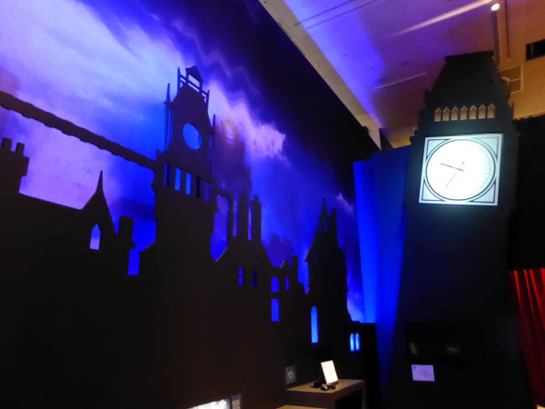 Decoration for the exhibition, showing a stylised, London skyline silhouetted black against a blue, night sky, with a stylished Big Ben with glowing clock face standing at an angle.