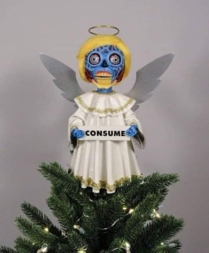 A tree topper on top of an Xmas tree but it's an alien from They Love in an angel costume holding a sign that says "CONSUME"