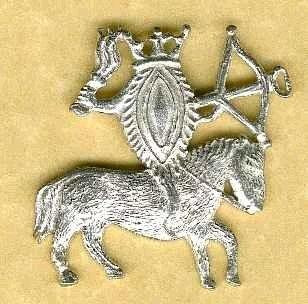 Silver badge of a stylised vulva on horseback, holding a flail and a crossbow. She is crowned like the queen she is.