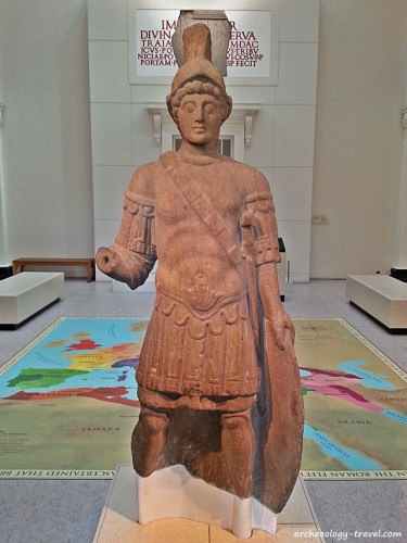 The sandstone statue of the god Mars is life-sized at 1.78 m (5'10'') and he is depicted as a youthful soldier, wearing a Greek helmet and a large oval shield is on the groun beside him, held by his left hand. He is wearing a muscle cuirass with elaborate lappets beneath and at the sleeves over a tunic. He has a sword strapped on his left side. His right arm is extended but the hand is missing: he probably held a spear originally. He is also missing the feet from below the ankle.