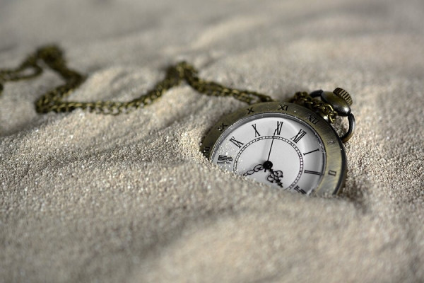 Photo of a pocket watch half-buried in sand.