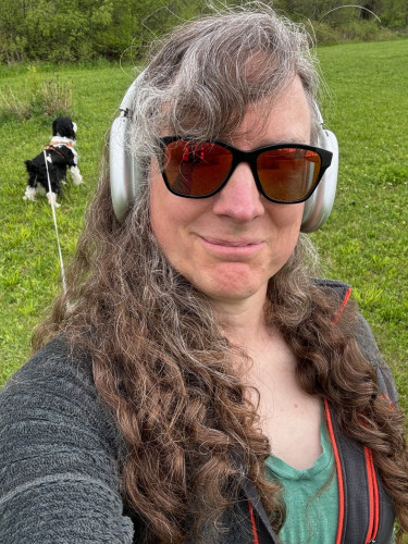 a selfie of me wearing mirror glasses, with a field of grass & our black and white dog behind me. 
