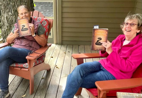 Two ladies sitting on a porch each hold up their copies of the book Hooper's Junction