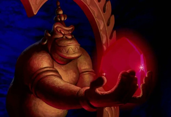 Screenshot of an animated film. A grinning stone figure holds a large, red gemstone.