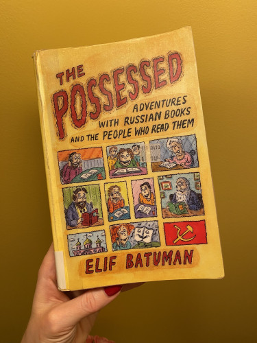photo of the cover of The Possesed: Adventures with Russian Books and the People Who Read Them by Elif Batuman. the title is in red letters on yellow background. The Possessed being a nod to a novel by Dostoyevskiy that is now in print as Demons. "People who read them" are displayed in comic panels as, well, people with books, reading. for some reason one of the panels shows a hammer and a sickle on red, like a soviet flag.