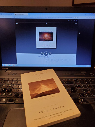 25th selection for The Sealey Challenge 2023 (reading 31 poetry works in the month of August): Novel in verse Autobiography of Red by Anne Carson (Random House/McClelland & Stewart) - the book sits on a computer keyboard, and on the computer screen is the book's audiobook version