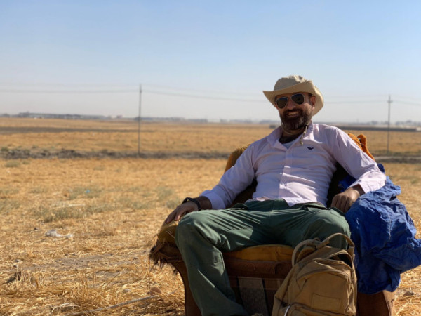 A photo of the archaeologist "Ako" sitting in an armchair on a field in Iraq.