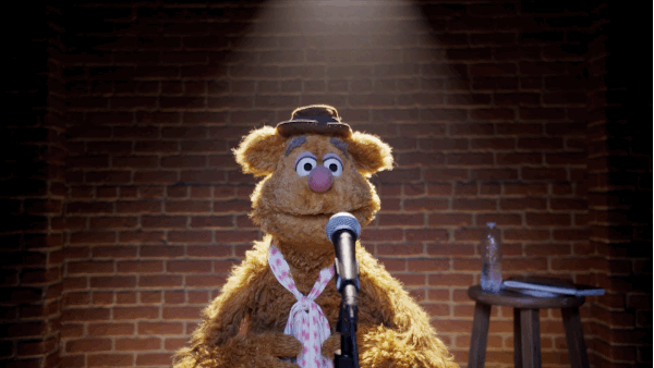Fozzy the Bear at a microphone, laughing at his own joke and getting lassoed from offstage.