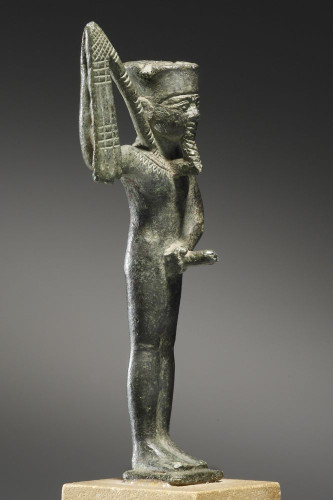 Dark stone figurine of Min holding a flail and his erect penis.