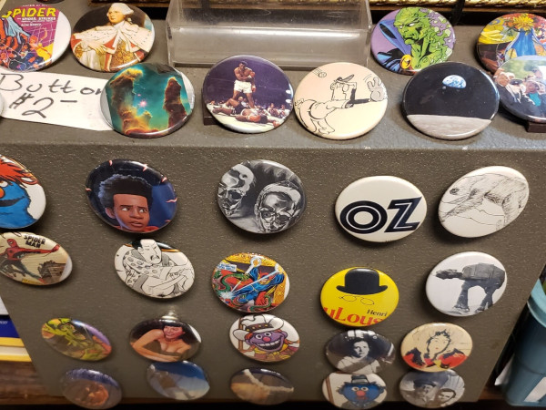 A photo of a display of many colorful pop-culture buttons. They're each circular, and 1.5 inches in diameter with a glossy face. The these craft items feature small images clipped from damaged vintage ephemera; such as: comic heroes, science images, famous personalities, works of art, logos, & more.