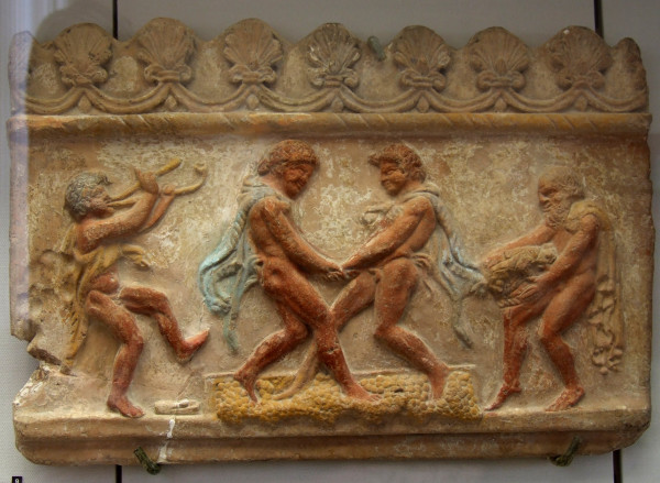 The two central satyrs hold hands and seem to dance upon the grapes. The satyr to the left plays the pipes; the satyr to the right holds a basket. The scene is bordered at the top by palmettes. Photo by shakko via Wikimedia Commons.