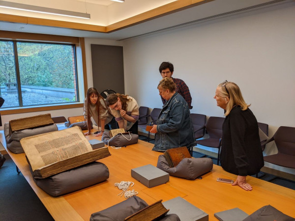 Four students and one lecturer looking at a parchment volume. Two Lambeth Bibles in the foreground 
