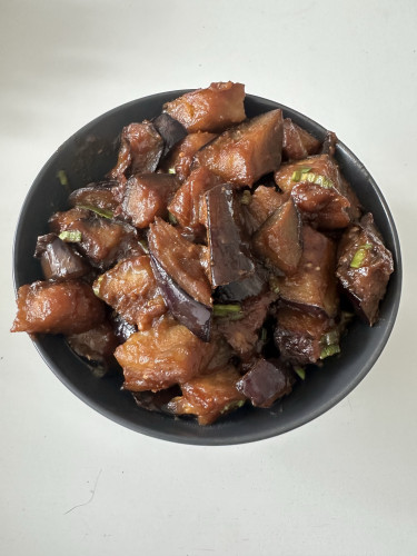 A photo of miso-glased eggplants in a black bowl. You can see there are eggplants with some brown glaze on them, there are bits of spring onions, but no sesame