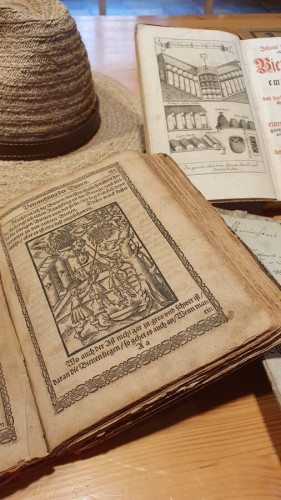 Das Bild zeigt verschiedene historische Drucke des 16. und 17. Jahrhunderts sowie einen Hut auf einem Tisch.