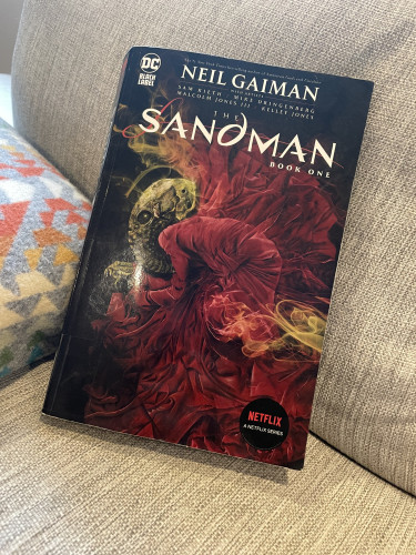 A copy of Neil Gaiman’s The Sandman, Book One propped up against a blanket on a couch. 