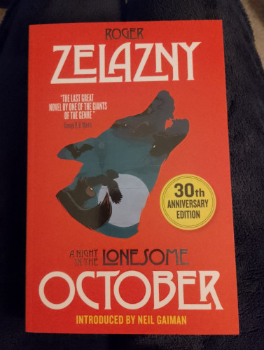 Bright orange book cover with the outline of a wolf's head in the middle. Inside the outline it is dark blue with black bats, cats, rats and owls and a pale blue full moon. The title of the book is A Night In The Lonesome October, the author is Roger Zelazny. At the bottom it says introduced by Neil Gaiman.