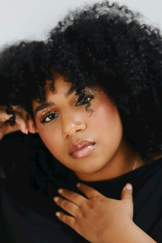Tight shot of a beautiful Black woman’s face and her abundantly curly raven mane.