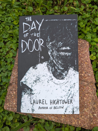 Paperback of THE DAY OF THE DOOR by Laurel Hightower. A decaying and dessicated-looking figure with a rictus of large white teeth is on the cover.