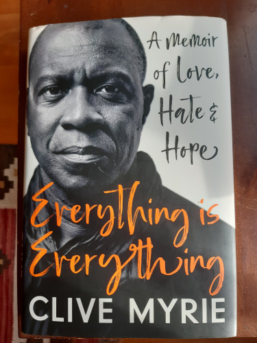 Book cover: head-and-shoulders photo of the author looking straight at the camera. Title in orange 'handwritten' font. 