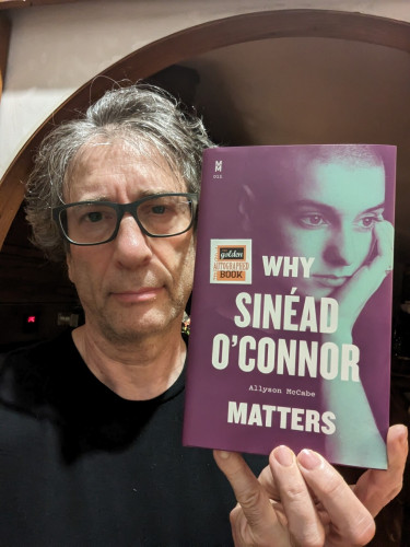 Sad author holding a copy of Why Sinead O'Connor Matters by Allyson McCabe