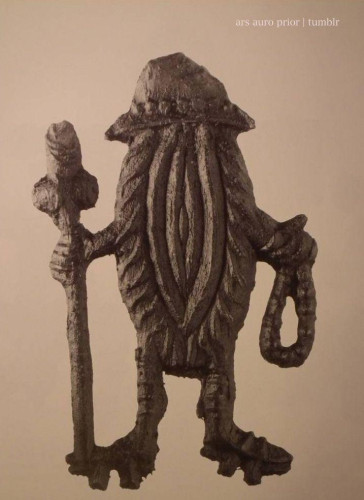 Pewter badge of a stylised vulva wearing a traveller's hat and carrying a walking stick and rosary like a pilgrim.