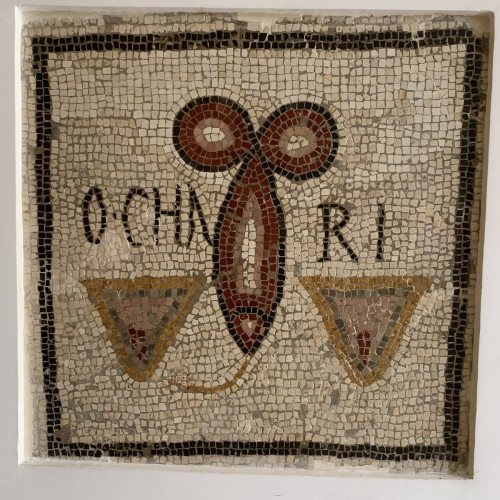 A mosaic depicting two vulvas as flesh-coloured triangles with a slit and a dark phallus between them. A lines goes from the tip of the phallus to the left vulva.