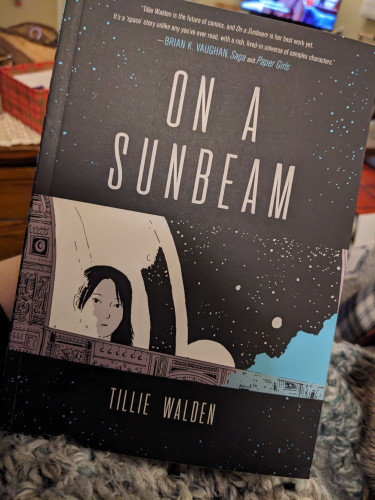 The cover of On a Sunbeam by Tillie Walden: a drawing of a girl looking out the window of a spaceship.  The style is cartoonish and it is mostly black and white, with a few teal stars one streak of teal in the lower corner.