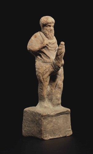 A terracotta statuette of the god Priapos with a huge erection. He is depicted with a full beard and seems fully dressed, the phallus emerging from below his chiton.