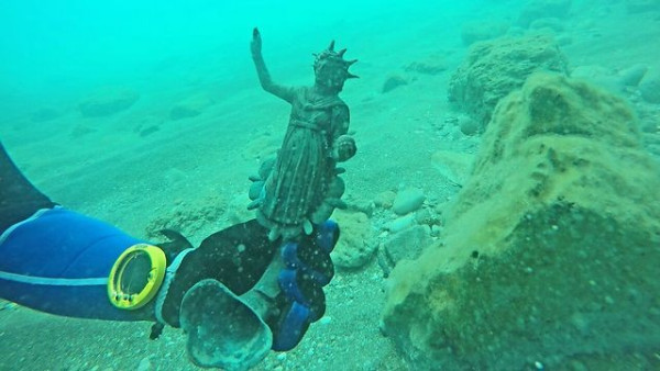 Underwater photo of diver holding a Roman bronze lamp of Helios-Sol. The god raises his right arm and holds a globe.