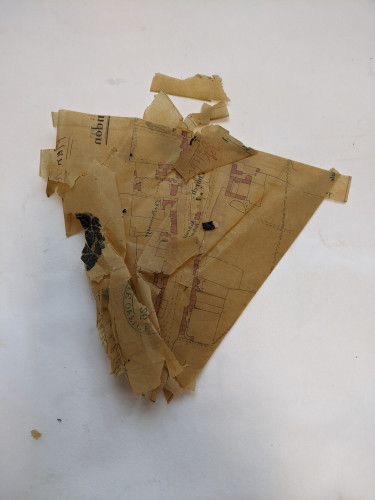 A light brown triangular-ish shape of creased and folded tracing paper with red ink, black ink, black sealing wax.