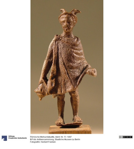 Roman bronze statuette of the god Mercurius or Mercury, holding a money purse. He is wearing a winged hat and chlamys cloak that reaches to his knees. He probably used to hold a caduceus staff too but it is now lost.