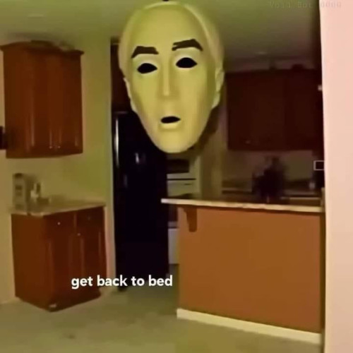 A giant face mask appears to hang in the air of an apartment with text that says "get back to bed"